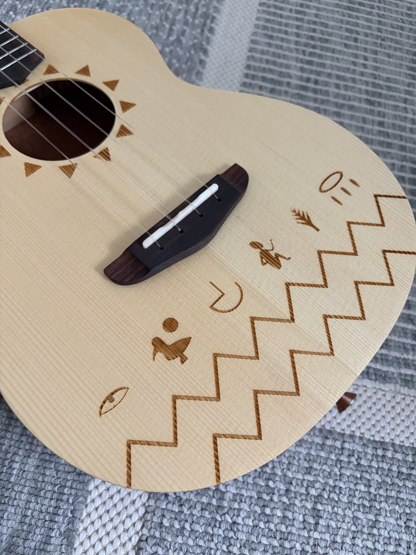 Nahaufnahme der TODO-Ukulelendecke mit Sonnenrosette, dunklem Steg und heller Stegeinlage
